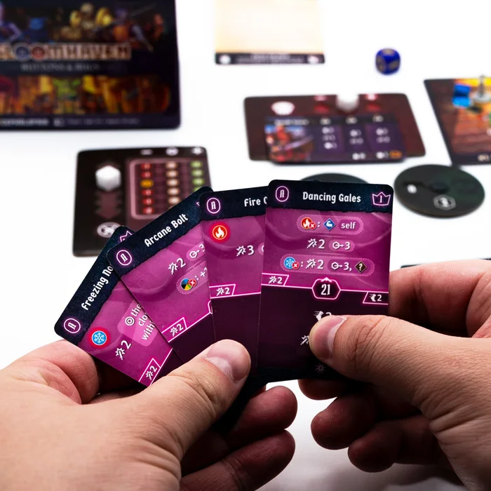 Two hands holding a spread of Buttons & Bugs ability cards over the game board, with the box behind.