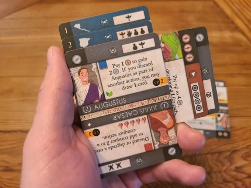 A hand holding a fan of Behold: Rome cards, with Augustus and Julius Caesar on top.
